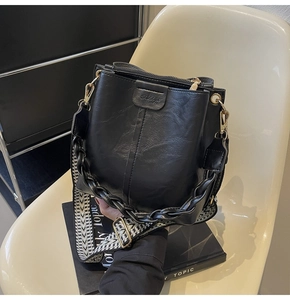 Detail view of black bucket bag with thick chain and woven V-pattern shoulder strap