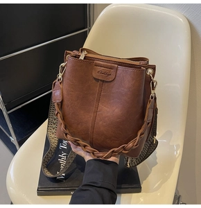 Detail of brown leather bucket bag with braided handle and ethnic style strap