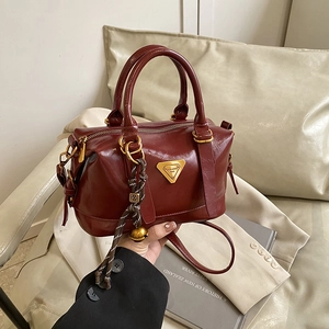 Deep red Boston style leather handbag on beige sofa with minimalist aesthetic decor