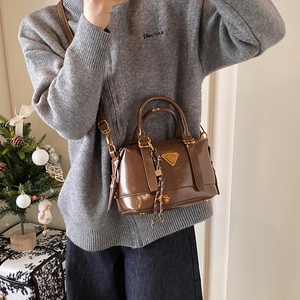 Brown patent leather satchel bag with gold hardware and woven charm accessory