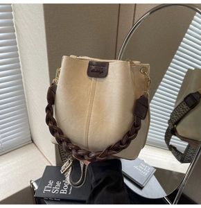 Detail of cream bucket bag showing woven leather handle and geometric woven shoulder strap
