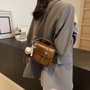 Brown leather crossbody square bag with baseball charm shown from a side view on model