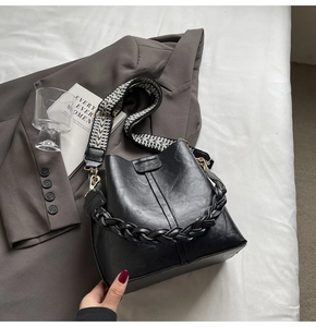 Close-up of black PU bucket bag featuring a geometric woven strap and braided handle