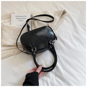 Detail of a black patent leather bowling bag with twin handles and a long shoulder strap
