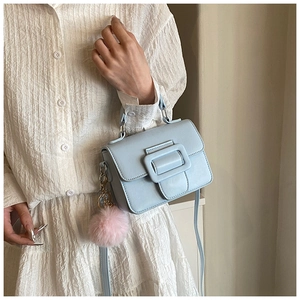 Dettaglio borsa a tracolla azzurra con ciondolo a pompon rosa e vestito bianco