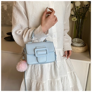 Dettaglio borsa azzurra con pompon rosa e fibbia quadrata su vestito bianco elegante