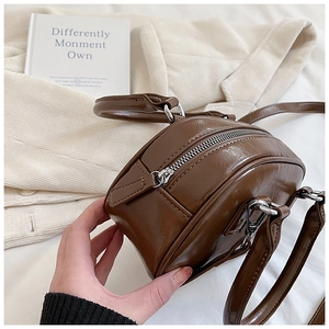 Detail view of the brown glossy mini round bag with silver hardware and zipper