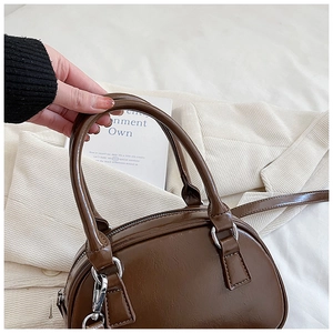 Close-up of brown glossy leather bowling bag with silver hardware and detachable strap