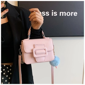 Dettaglio di una borsa quadrata rosa pallido con fibbia grande e ciondolo a pompon blu