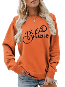 Detail of orange crewneck sweatshirt featuring a black Believe Nativity graphic print
