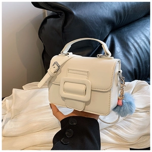 Dettaglio mini borsa bianca con grande fibbia quadrata e ciondolo a pompon blu laterale