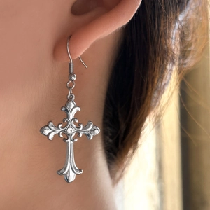 Close-up of gothic vintage silver cross earrings with clear crystal and engraved texture
