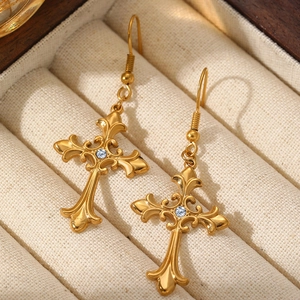 Macro detail of gold gothic cross earring with central crystal on beige texture