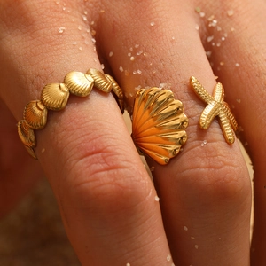 Detailed macro shot of adjustable gold starfish and shell rings on a sandy background