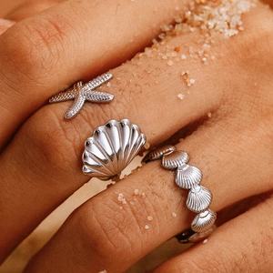 Detail of three starfish and seashell silver rings set with sand background for summer