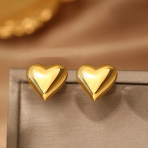 Macro shot of polished gold heart stud earrings on a metallic display stand