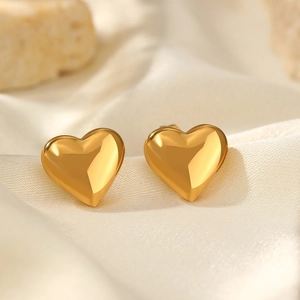Polished gold heart studs displayed on elegant wrinkled beige silk fabric background