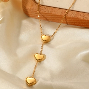 Detail of gold-plated triple heart pendant necklace displayed on white silk and wood