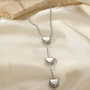 Minimalist stainless steel necklace with triple heart pendants on silk fabric