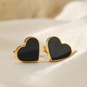 Macro detail of gold heart earrings with black enamel on light beige silk fabric