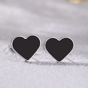 Macro shot of silver heart studs with black onyx centers on textured stone surface