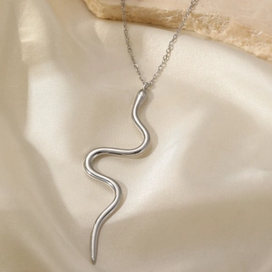 Gros plan du pendentif serpent argenté poli sur fond de pierre et de soie