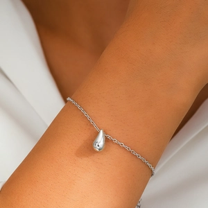Detailed close-up of a minimalist silver teardrop pendant on a fine link chain bracelet