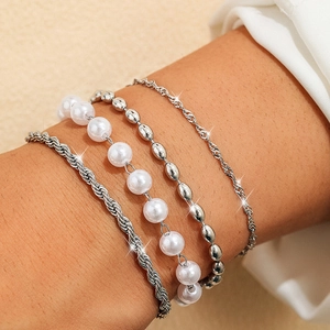 Dettaglio del set di quattro bracciali a catena argentata con perle finte sul polso