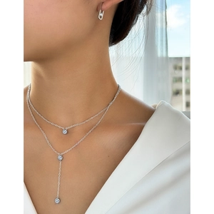 Close-up of double-layer silver necklace and geometric diamond earrings on a model