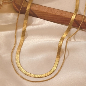 Macro detail of double-layered 18K gold snake chain necklace on white silk fabric