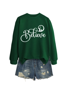 Flat lay of a green crewneck sweatshirt with 'Believe' print and denim shorts