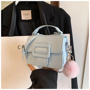 Dettaglio mini borsa quadrata celeste con fibbia e ciondolo pompon di pelliccia rosa