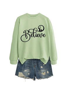 Flat lay of a light green crewneck sweatshirt with Believe nativity print and denim shorts