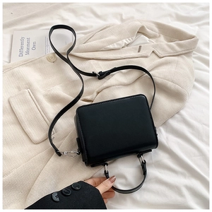 Dettaglio di una borsa a mano nera opaca su un blazer beige con finiture metalliche argentate