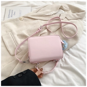 Dettaglio borsa a tracolla rosa chiaro con pompon blu su sfondo di lino bianco