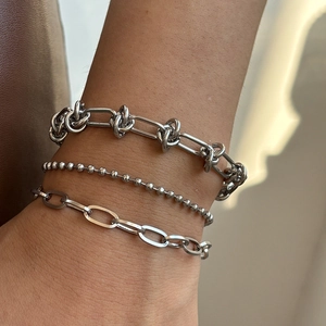 Close-up of stacked silver metal bracelets featuring knot, bead, and oval link textures