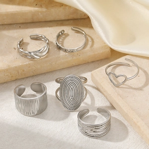 Detailed view of six vintage silver-tone open rings on a stone surface with beige fabric