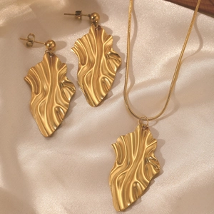 Detailed view of golden rhombus leaf earrings and necklace set on satin background