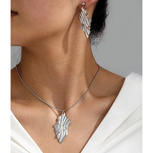 Close-up of woman wearing silver leaf-shaped textured jewelry set with necklace and earrings