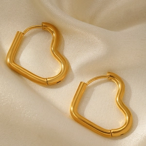 Détail de boucles d'oreilles cœur en or mat avec fermoir huggie sur fond soie