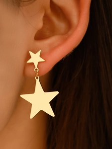 Close-up of golden star-shaped tassel earrings worn by a model in warm lighting