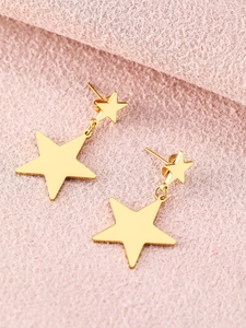 Close-up of golden double star tassel earrings on a textured soft pink fabric background