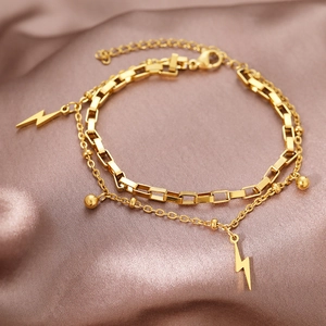 Detail of gold double-layer chain bracelet with lightning pendants on purple satin