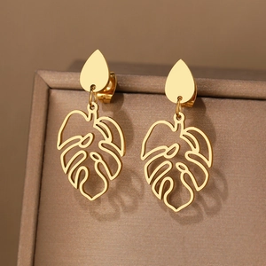 Vue macro de boucles d'oreilles en acier doré avec pendentif feuille ajourée sur support