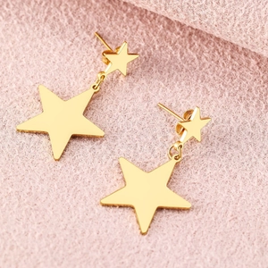 Minimalist gold star fringe earrings with polished finish on a pink knitted fabric background