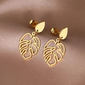 Boucles d'oreilles monstera en acier inoxydable doré sur fond de soie champagne