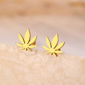 Detail shot of golden maple leaf stud earrings on a beige textured stone stand
