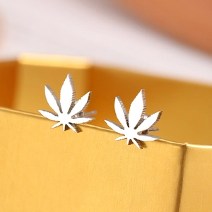Macro detail of silver maple leaf stud earrings resting on a golden luxury display box