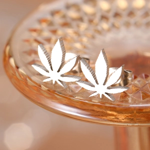 Macro view of polished silver maple leaf stud earrings resting on amber relief glass