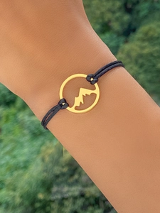 Close-up of golden mountain range pendant on adjustable black woven rope bracelet